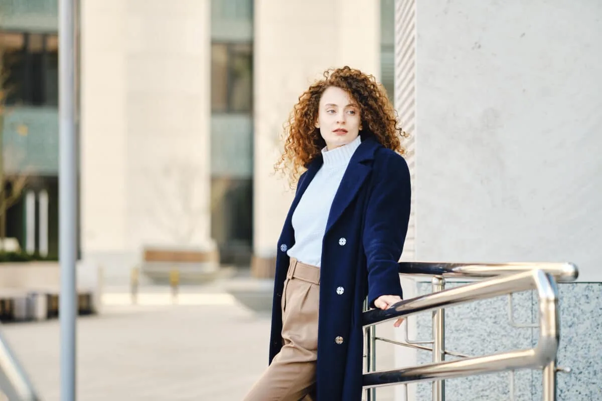Jeune femme en manteau en laine appuyée sur un garde-corps extérieur
