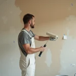Peintre professionnel en train d'appliquer de la peinture au rouleau sur un mur intérieur lors d'une rénovation appartement