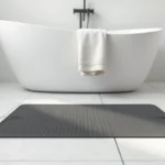 Tapis antidérapant design gris anthracite à motif géométrique devant une baignoire blanche dans une salle de bains moderne et minimaliste